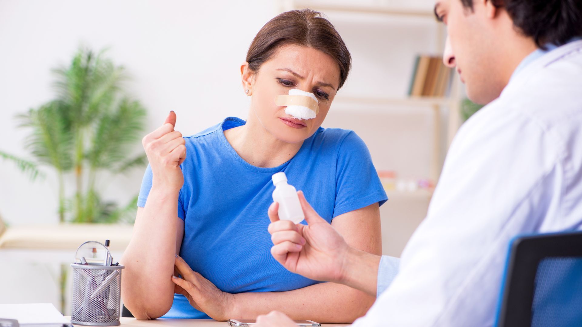 Woman with a nasal strip talking to a doctor holding a medicine bottle in a clinic