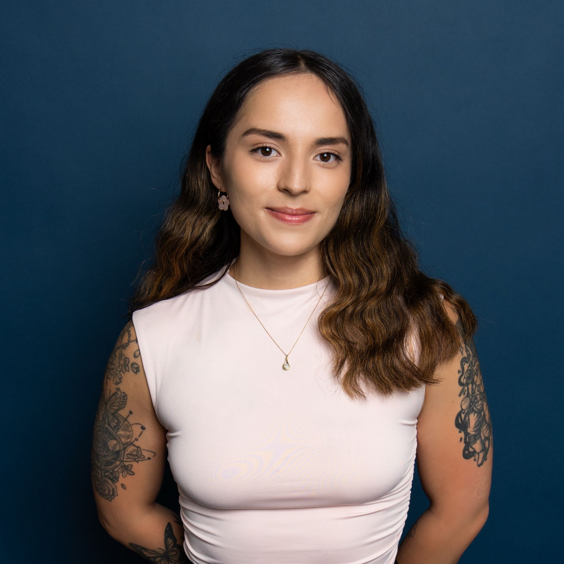 Portrait of a person in a light pink top against a dark blue background, smiling gently.