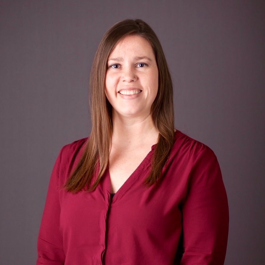 person smiling in a maroon blouse against a gray background
