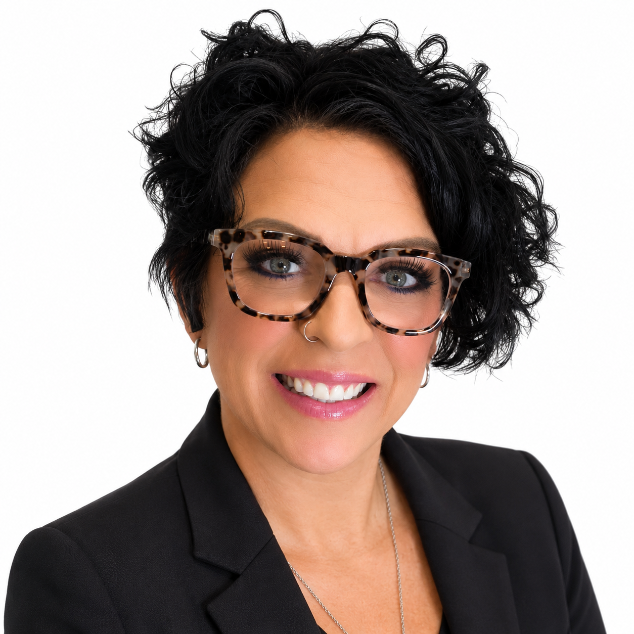 Headshot of a smiling person with curly black hair, tortoiseshell glasses, and a black blazer on a white background