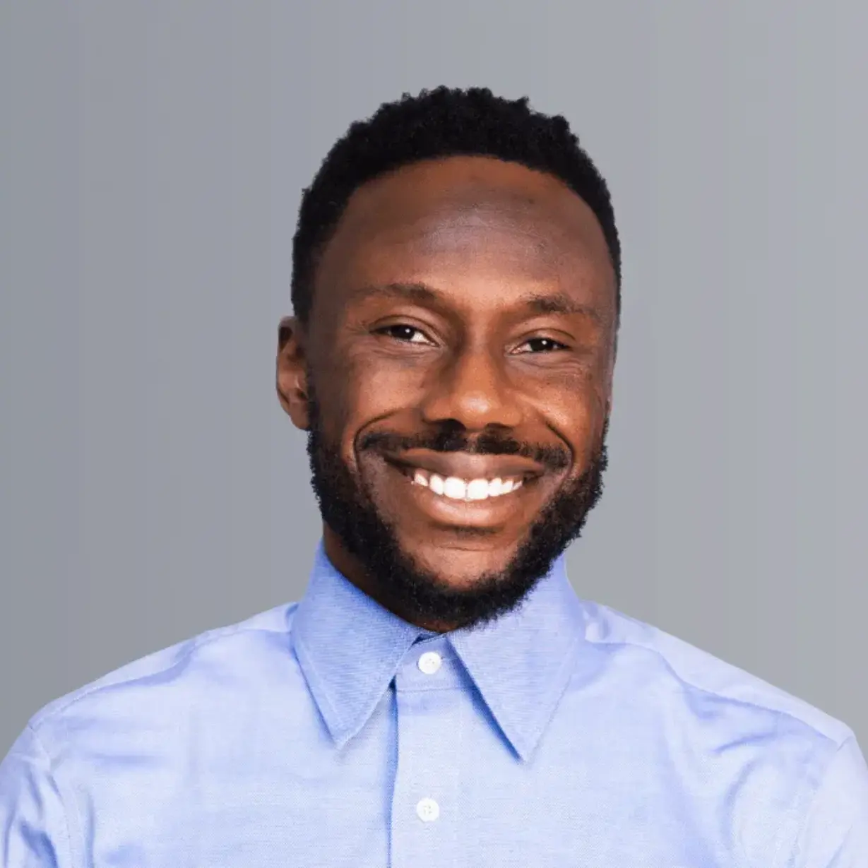 Smiling man in a light blue button-up shirt against a gray background