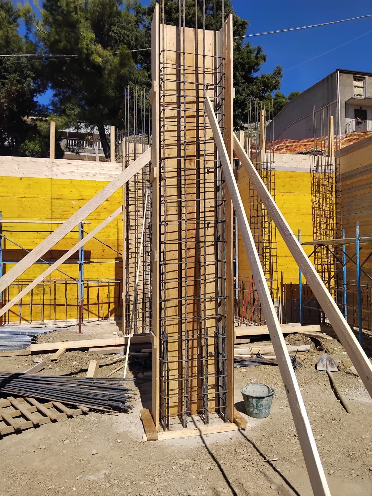 Gabbia di rinforzo in acciaio su base di legno in un cantiere edile, con un camion sullo sfondo.