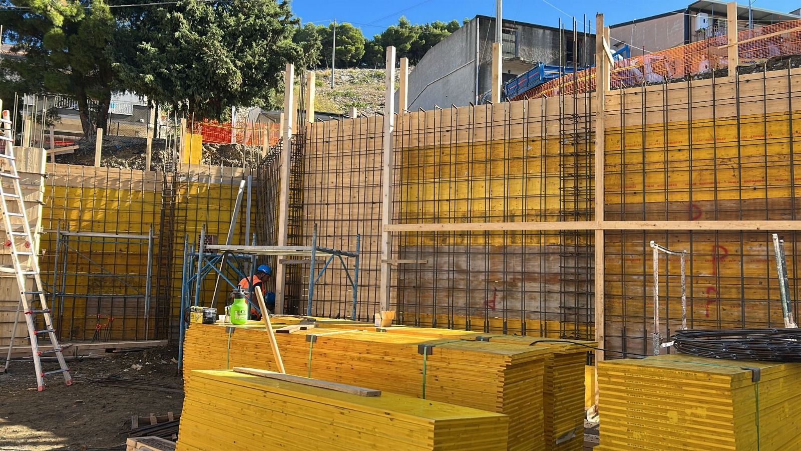 Cantiere con casseforme gialle, barre d'armatura e pannelli di casseforme impilati.