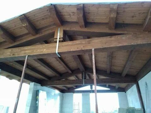Struttura del tetto in legno in costruzione, sostenuta da pali temporanei su un edificio in blocchi di cemento.