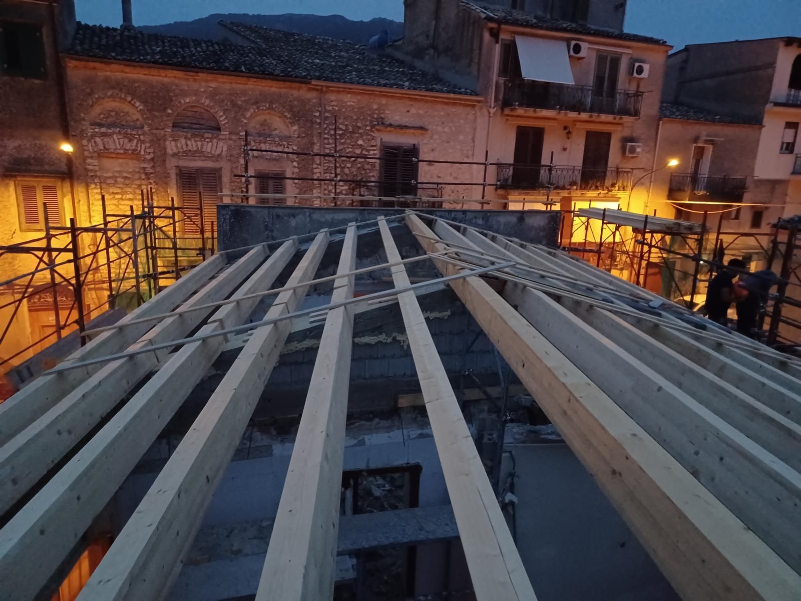 Travi di legno posate per la costruzione di un tetto in un contesto urbano al tramonto. Impalcature visibili.