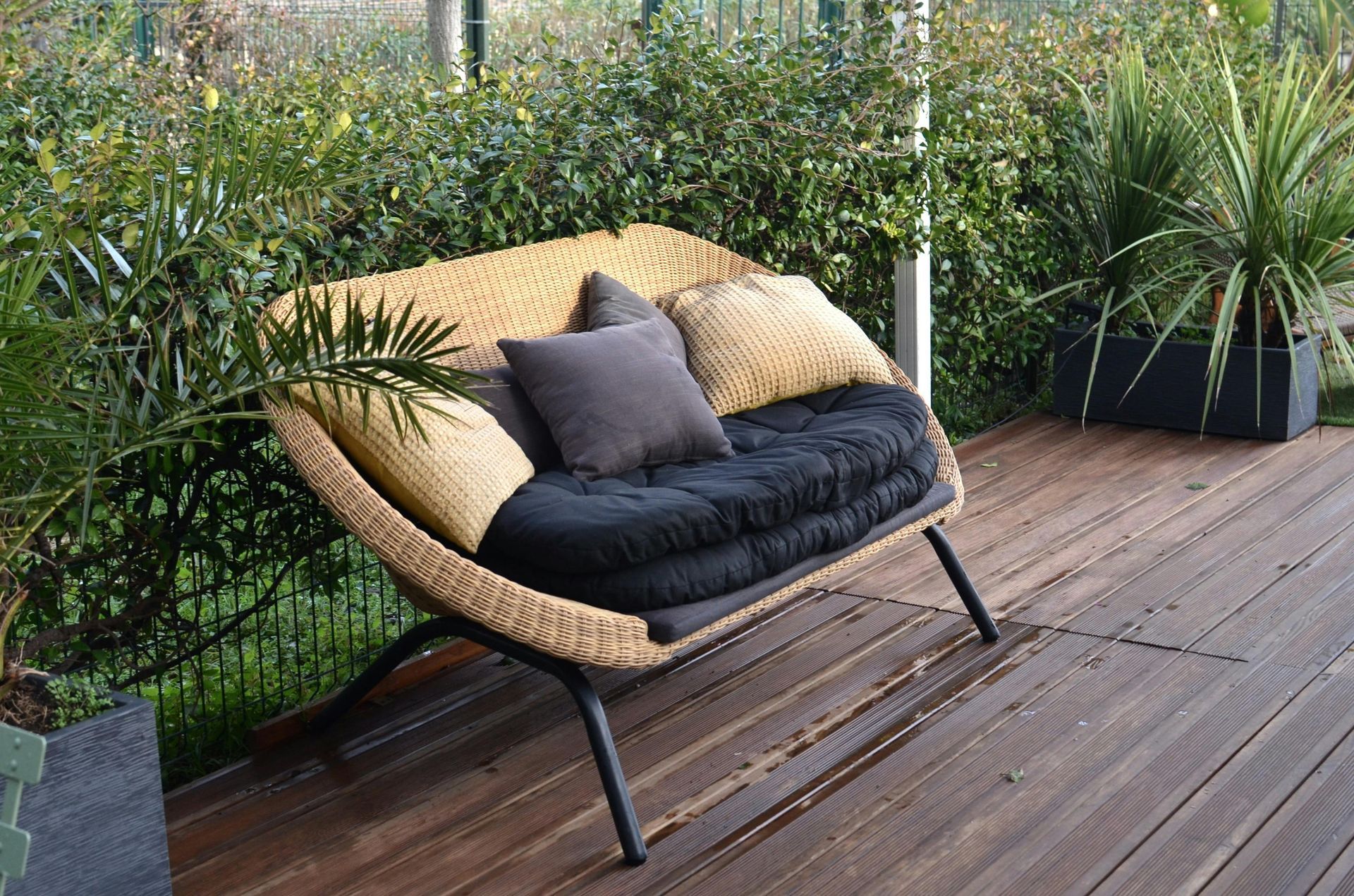A wicker bench with pillows on it is sitting on a panted wooden deck.