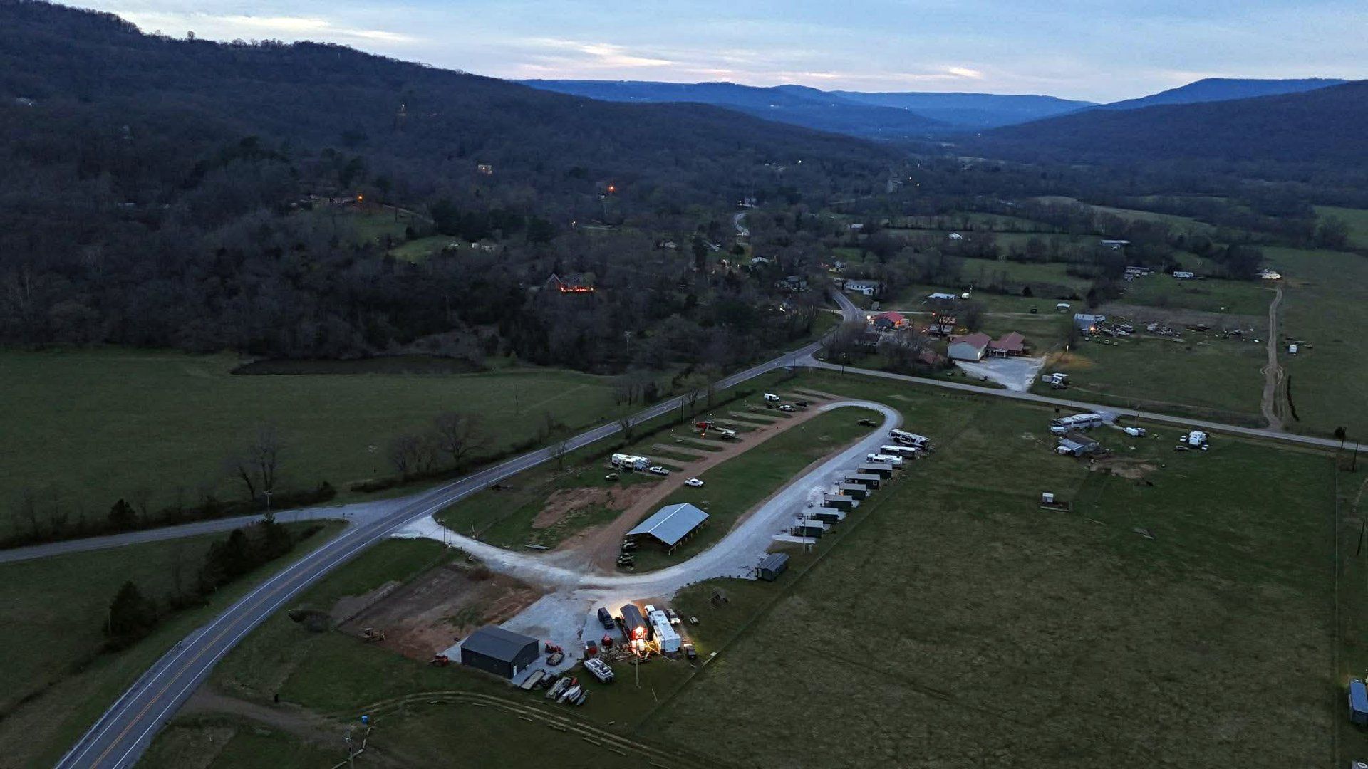 Aerial view of a rural campground with cabins, a road, and hills at dusk