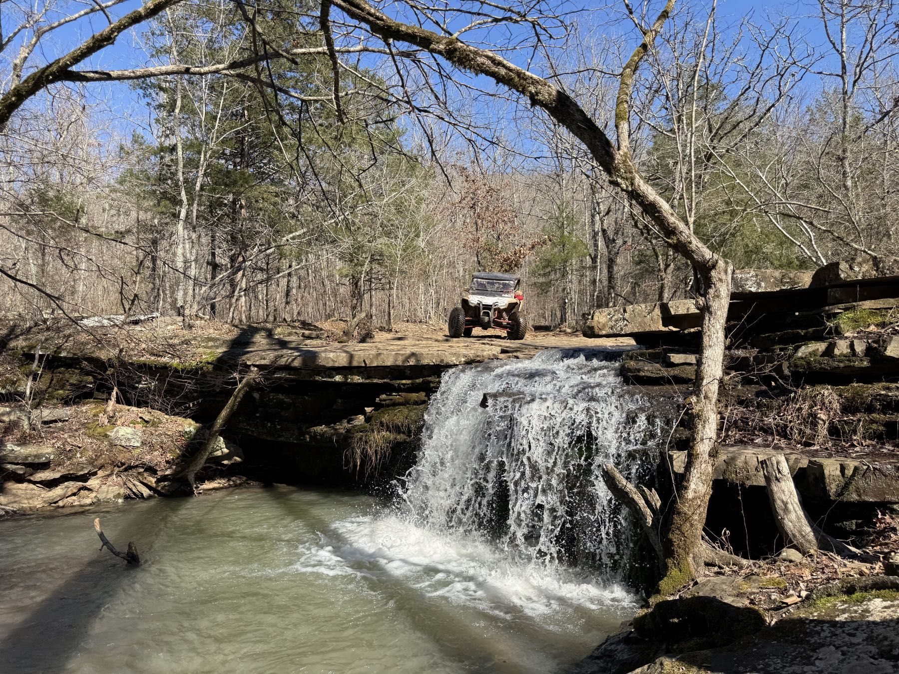 Small waterfall in a wooded area with an orange ATV parked above it