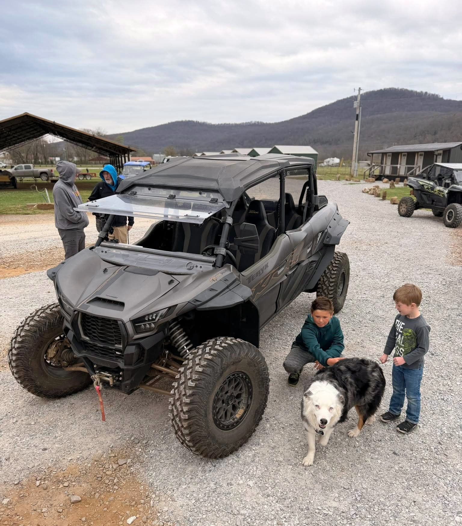 Black off-road UTV on gravel with two children and a dog in a rural mountain setting
