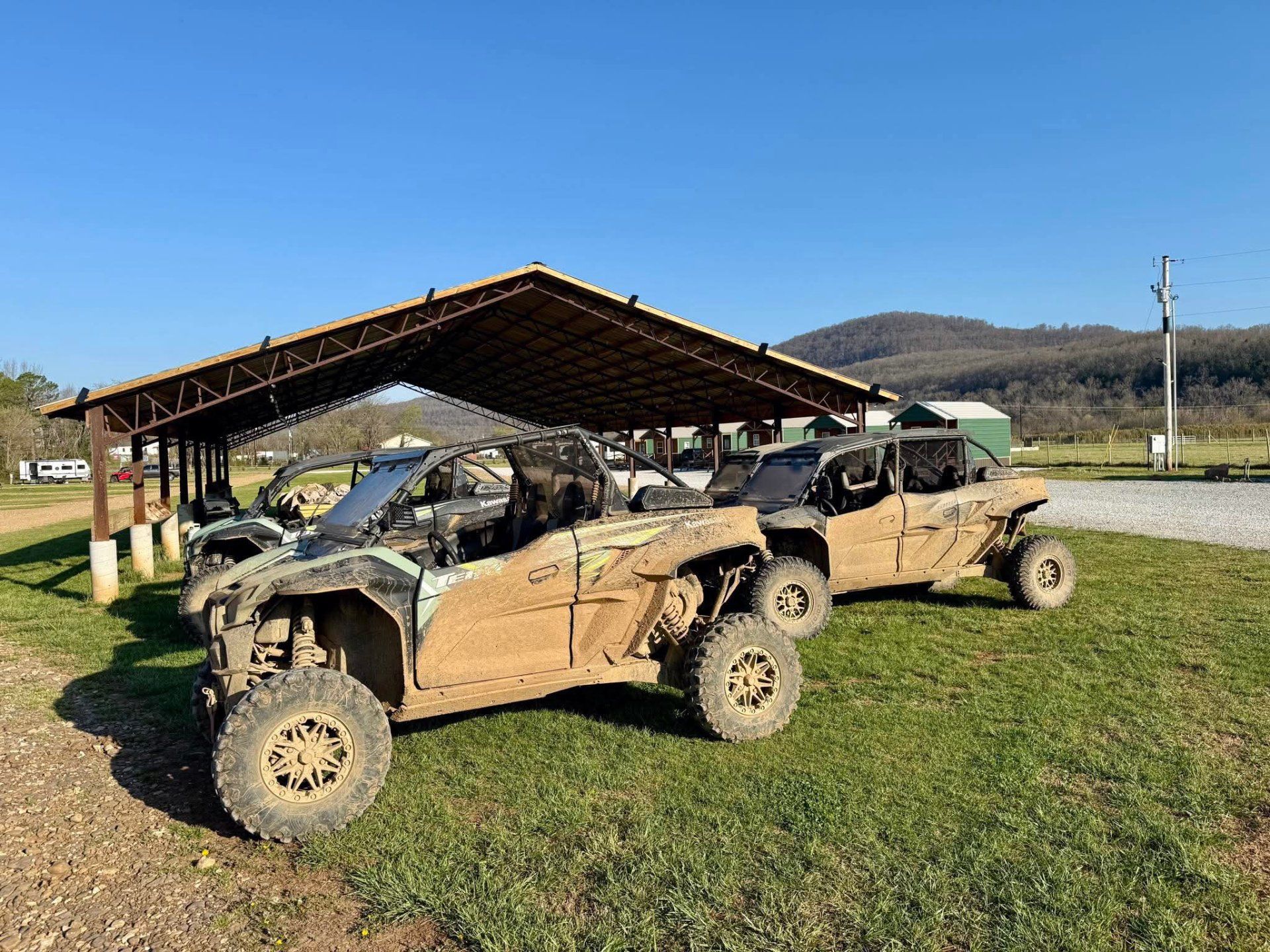 Two mud-covered off-road vehicles parked beside a metal shelter on a grassy field