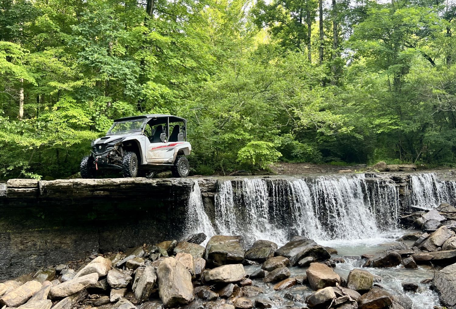 Off-road vehicle beside a small waterfall in a green forest