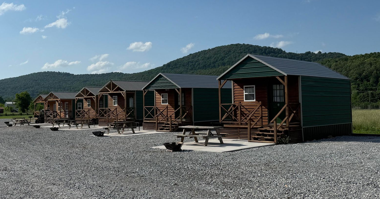 Row of rustic cabins on a gravel lot with mountains and blue sky in the background