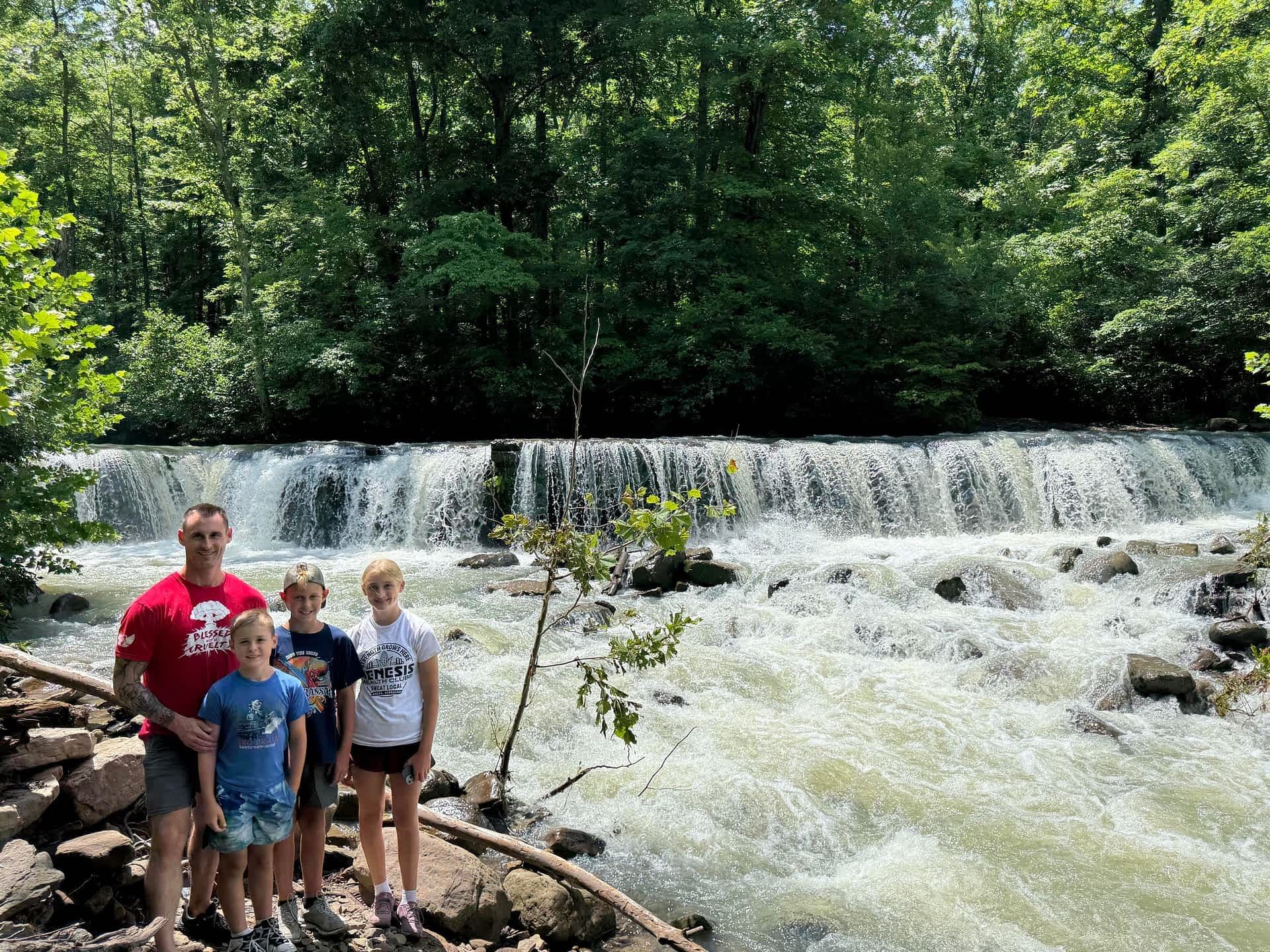 Family posing by a rocky waterfall in a forest; water rushing over the falls.
