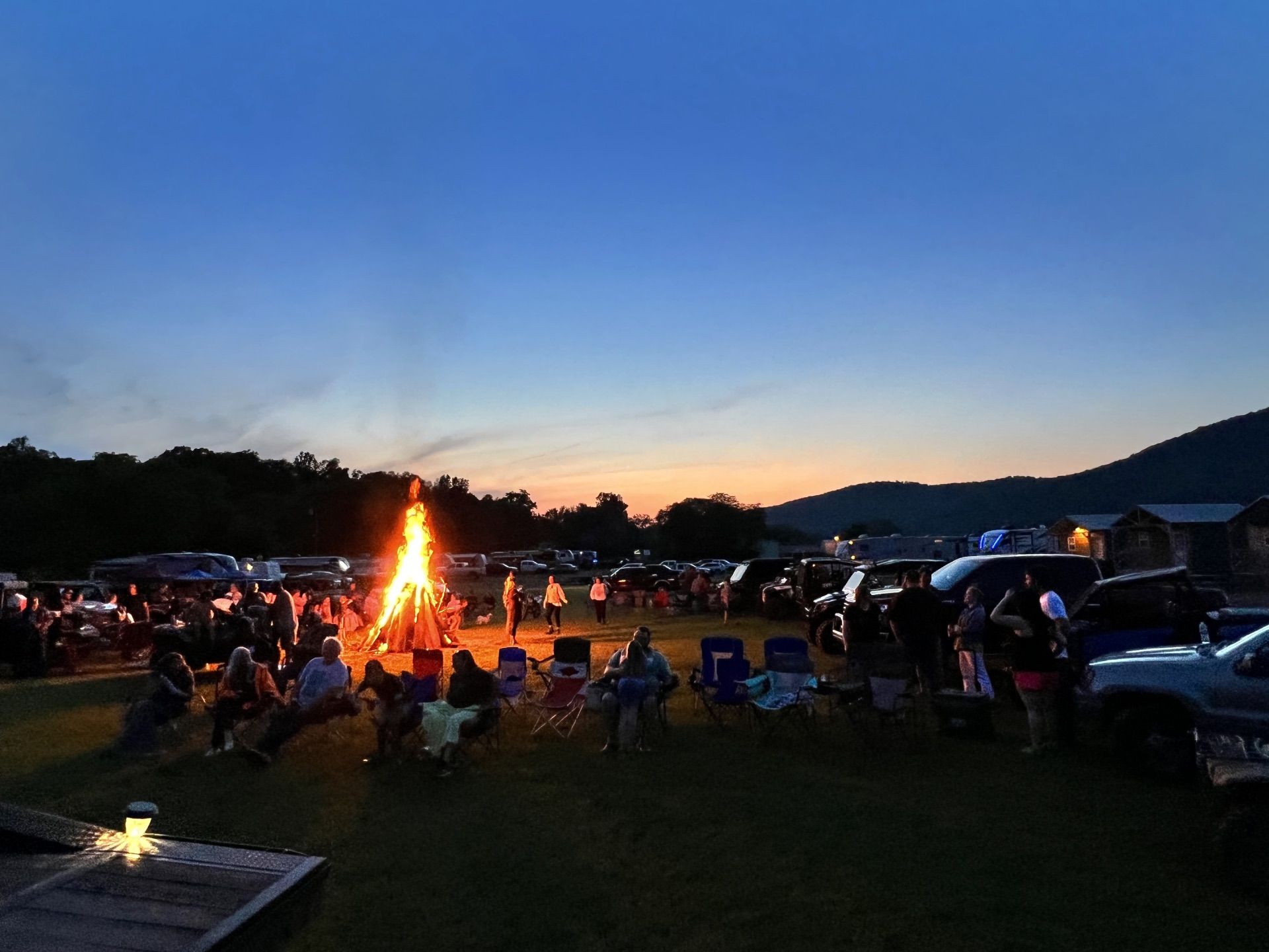 Crowd gathered around a bonfire at dusk in an open field under a blue evening sky