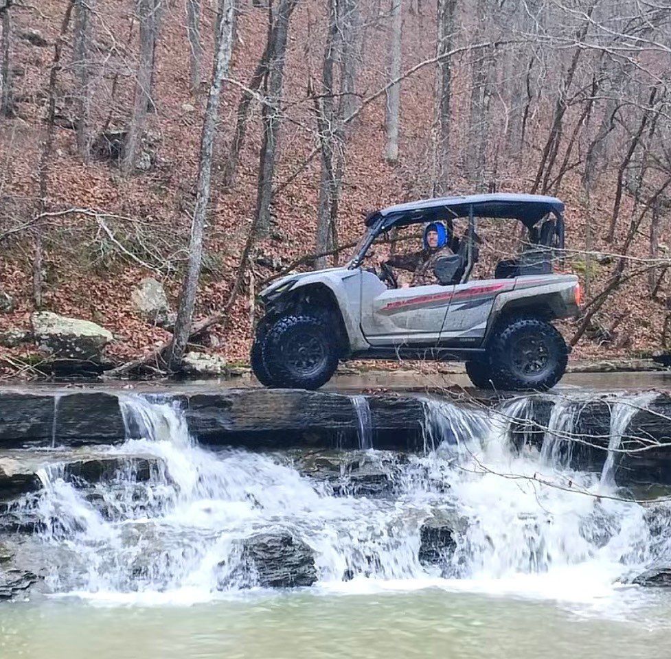 Off-road vehicle driving over a small waterfall in a wooded area