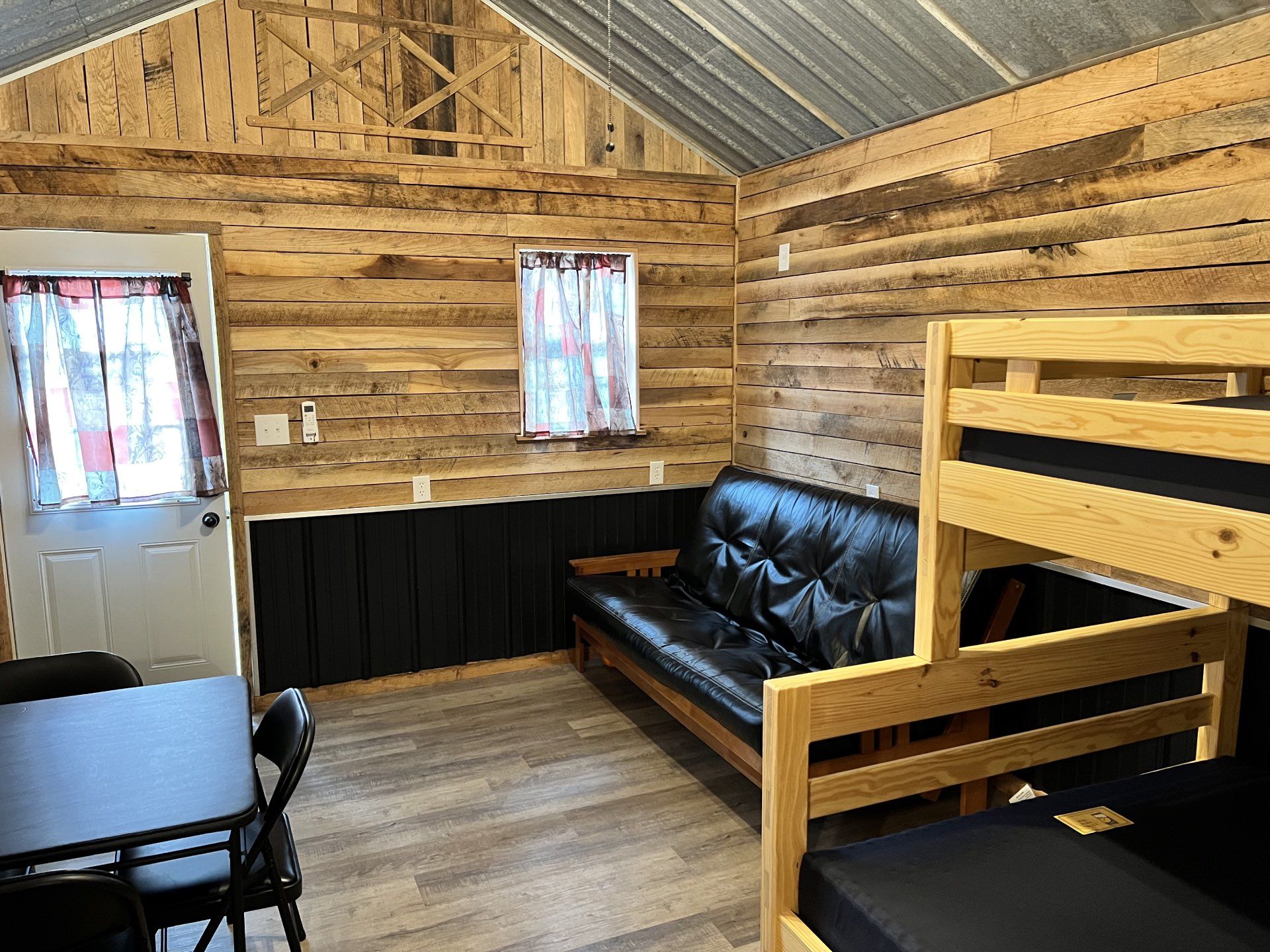 Rustic cabin interior with bunk beds, black couch, small table, and wood-paneled walls and ceiling