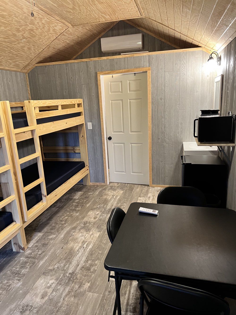 Small room with bunk beds, a white door, desk, and dark table under a sloped ceiling.