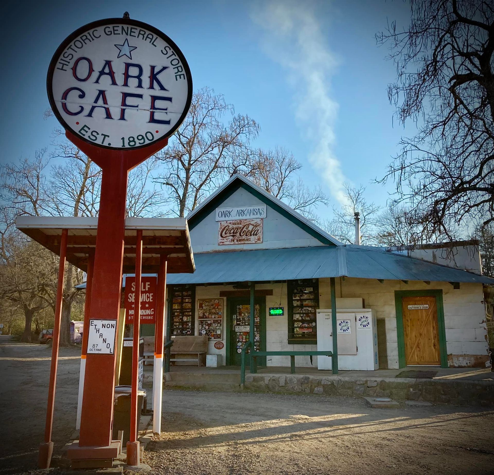 Oak Cafe storefront with round sign, red posts, and a weathered blue-roofed building at dusk