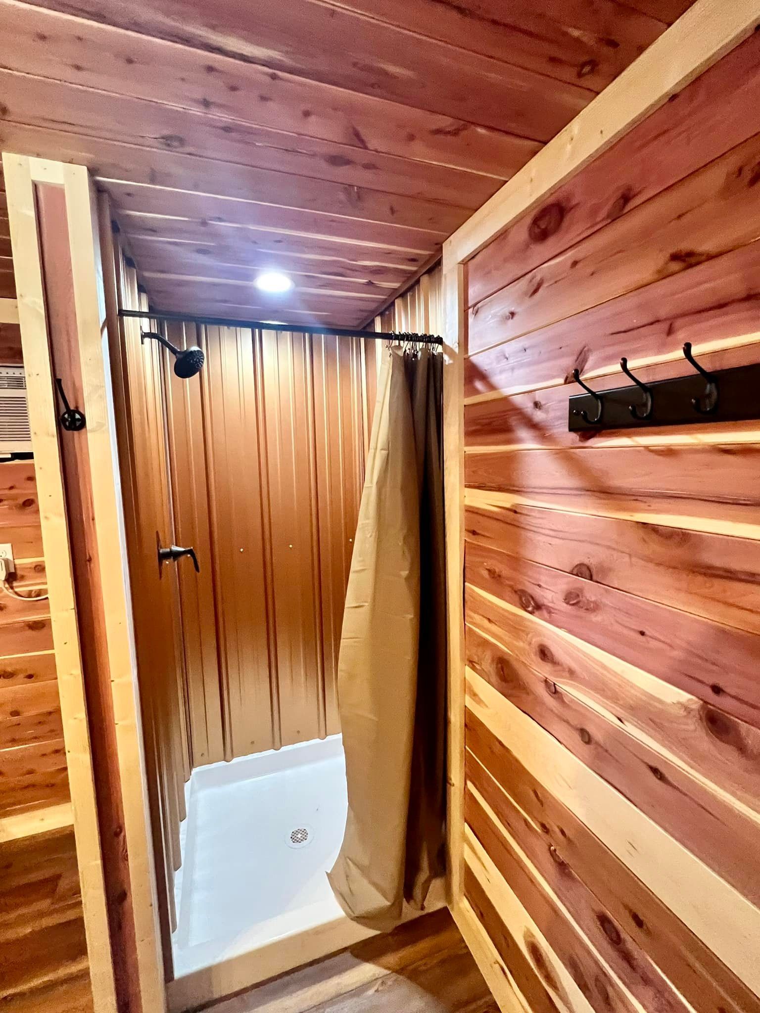Wood-paneled shower stall with a curtain in a narrow, rustic sauna-like bathroom.