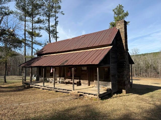 Rustic wooden cabin with a rusted metal roof and front porch in a wooded clearing