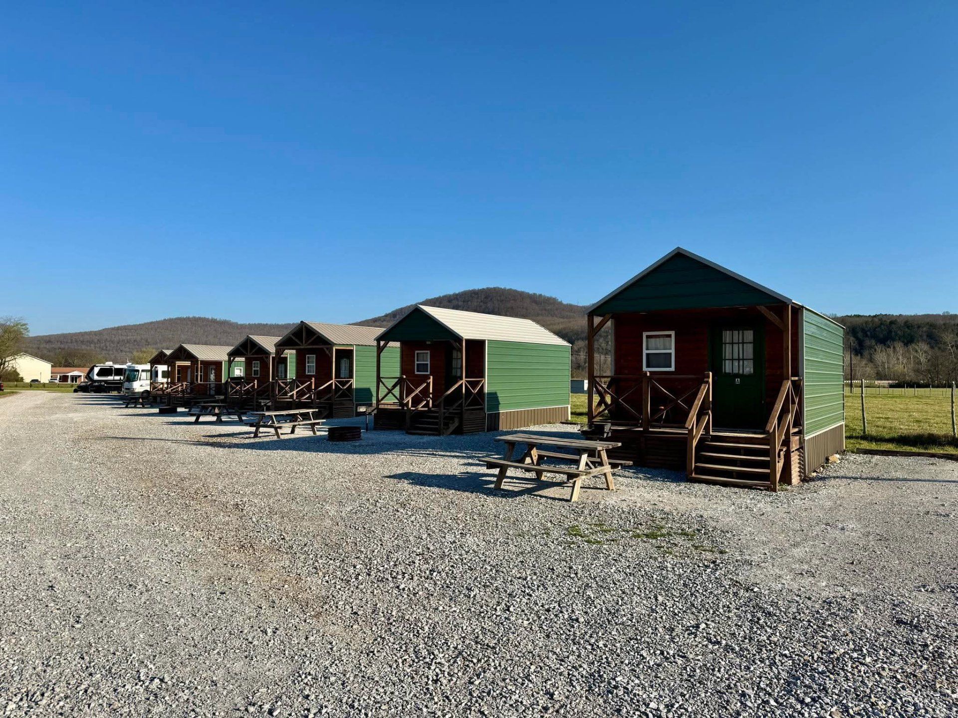 Row of small cabin rentals on gravel under a clear blue sky, with hills in the background