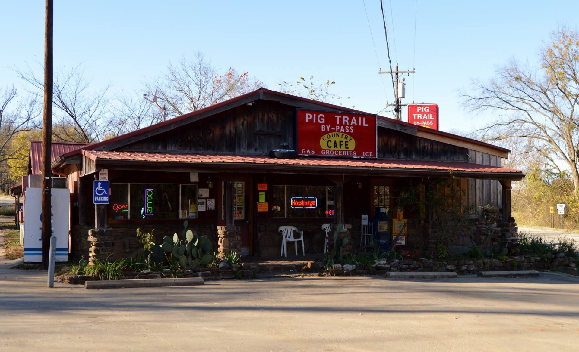 Small rustic roadside café with a red sign, porch seating, and trees in front