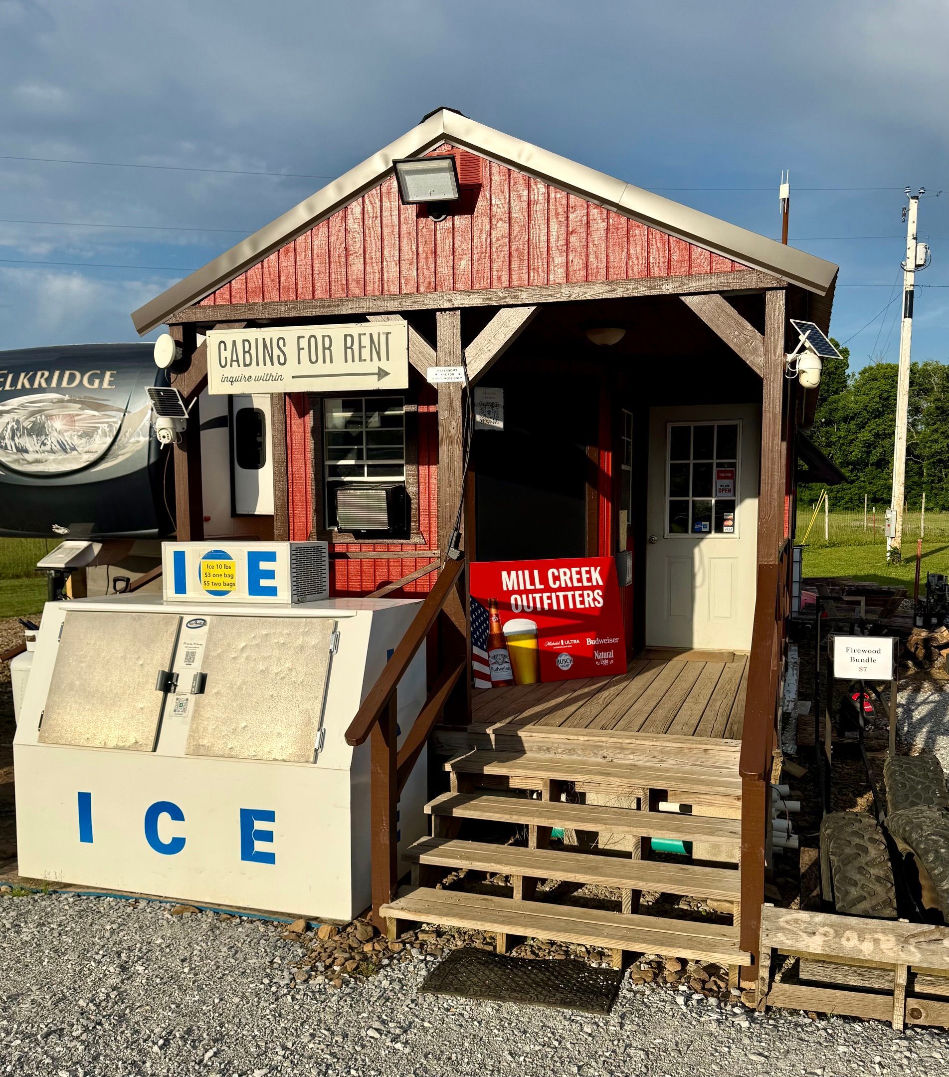 Small rustic seafood shack with a wooden porch, steps, and ice chest outside under a cloudy sky.