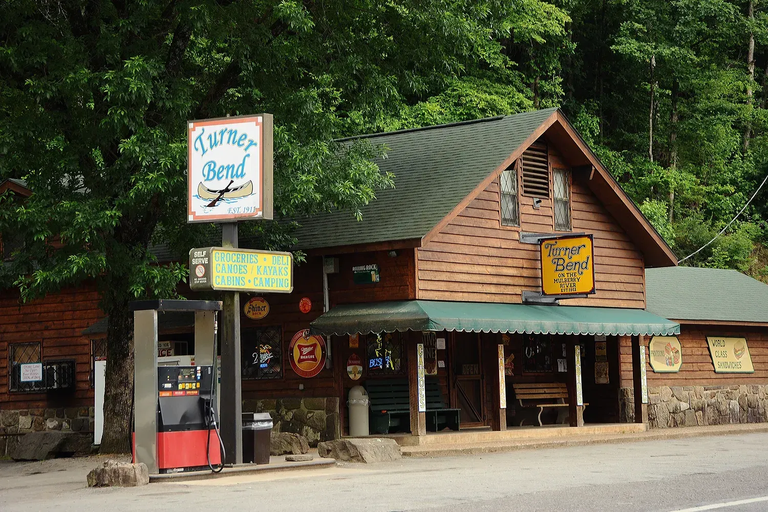 Rustic roadside shop with green roof, wooden facade, and colorful signs in a wooded setting