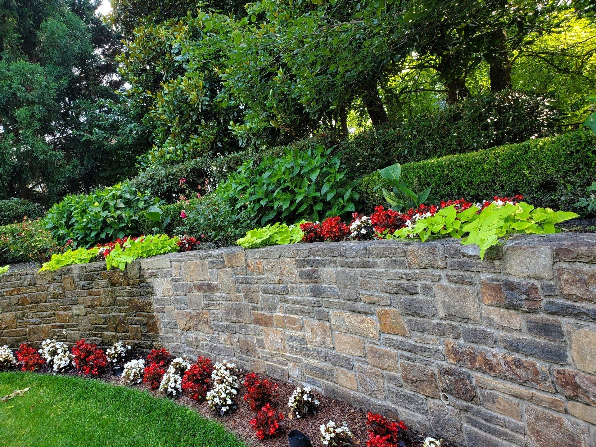 A stone wall surrounded by flowers and trees in a garden.