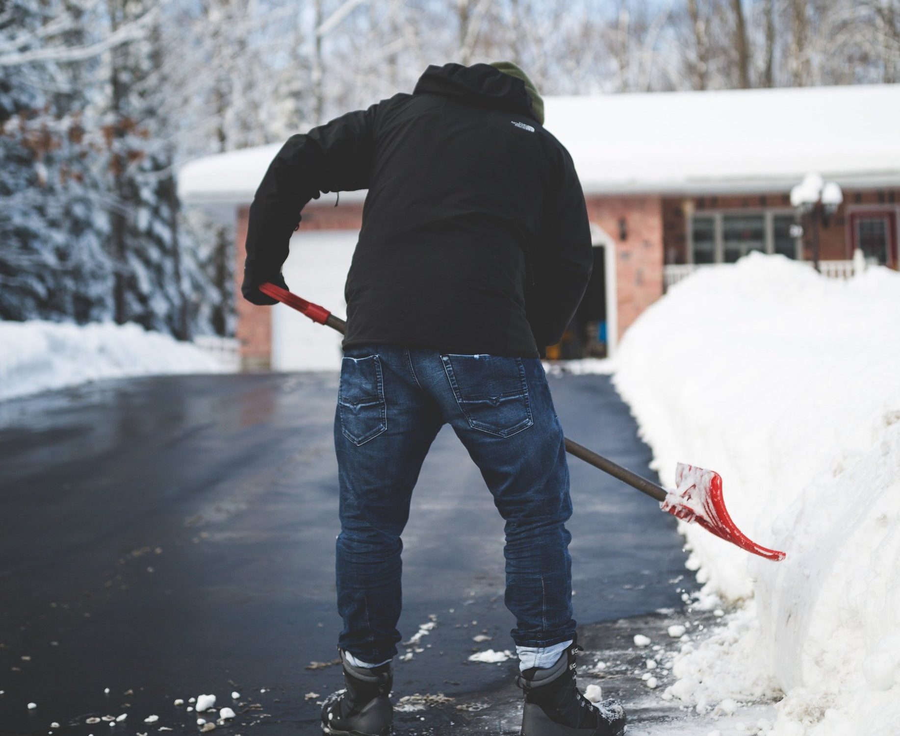 A man is shoveling snow from a driveway in front of a house.