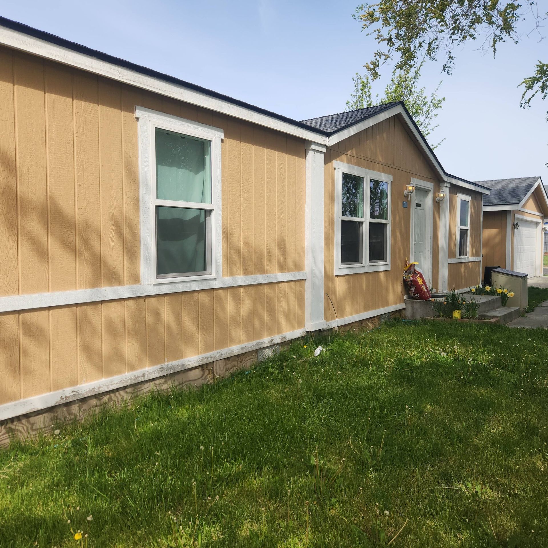 Yellow mobile home exterior with white trim, green lawn, and a small porch by the entry door