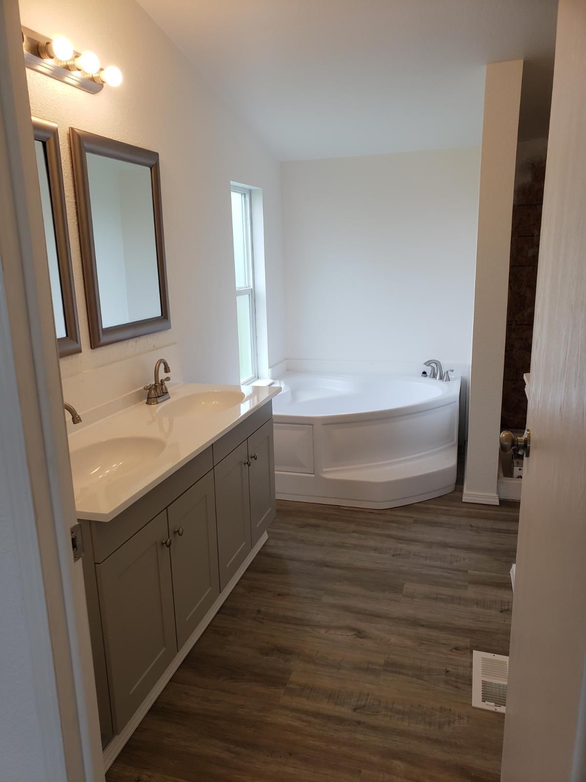 Bathroom with double vanity, mirrors, and a freestanding bathtub by a window.