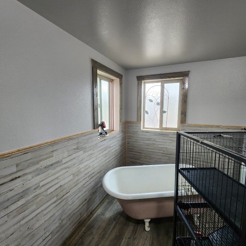 Bathroom with a freestanding tub, gray tile walls, and two windows letting in natural light
