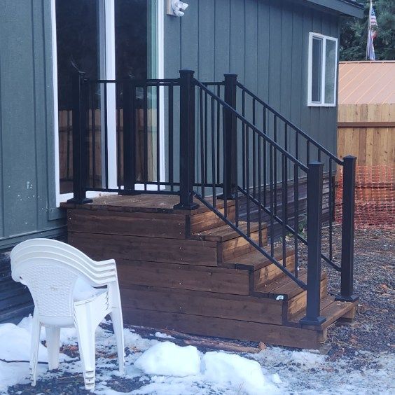 Snowy backyard deck with black railing, gray house siding, and white chairs.