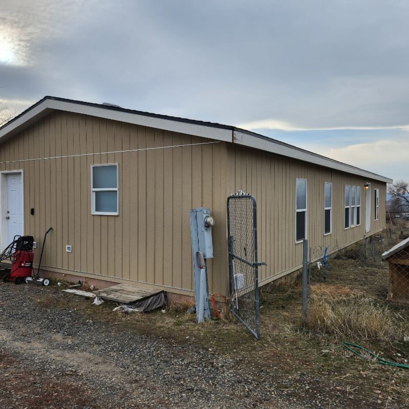 Tan beige single-story mobile home with white-trimmed windows and a gravel yard under cloudy skies