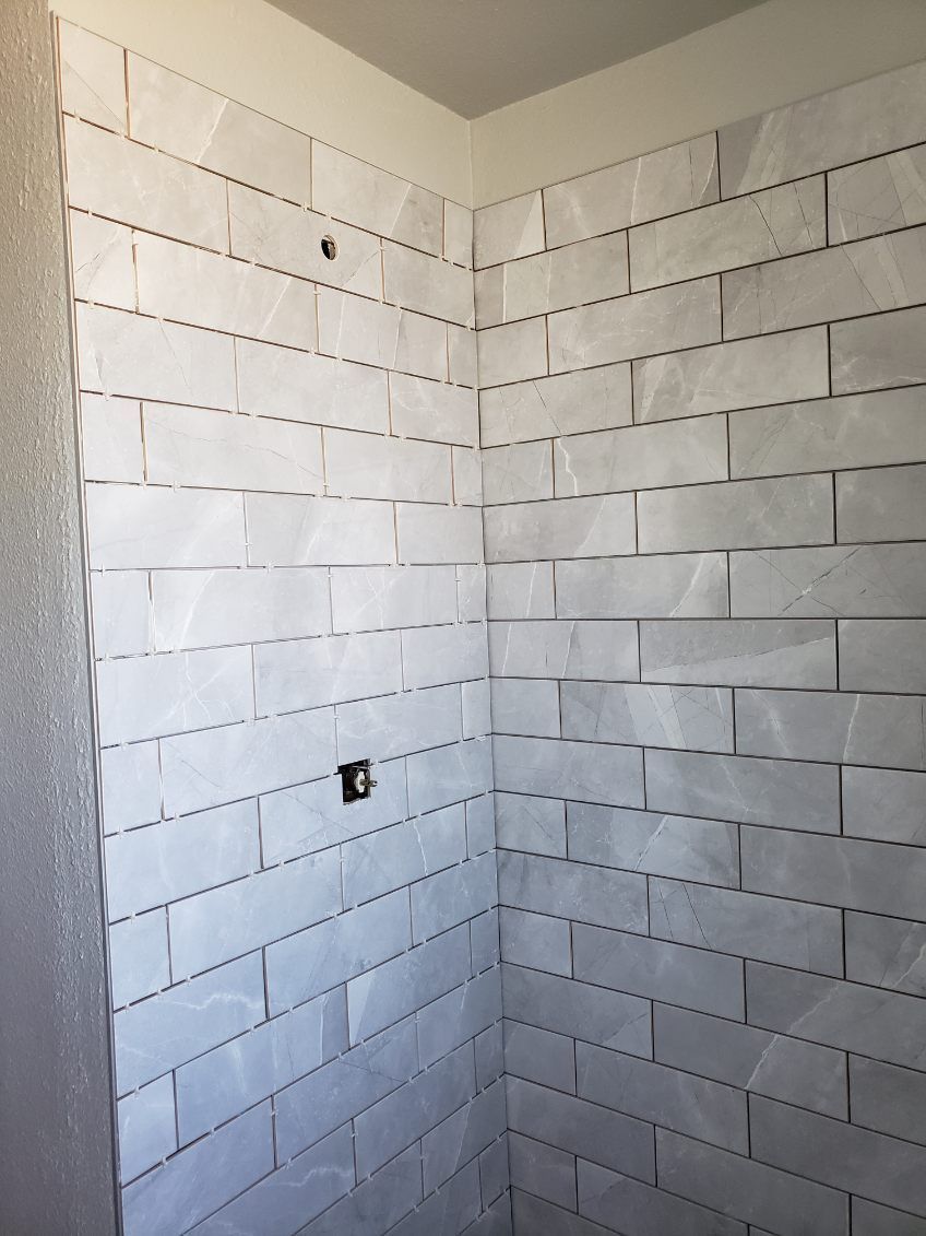 Freshly tiled white shower corner with staggered rectangular tiles and a single outlet opening