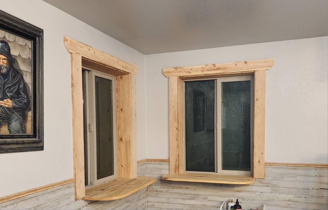 Two unfinished wood-framed windows in a white room, with a framed painting on the left wall.