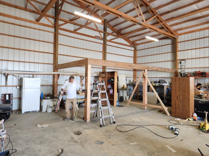 Person standing in a large unfinished workshop with ladders, tools, and exposed beams