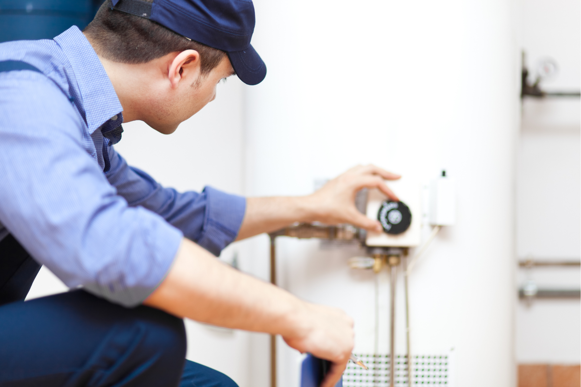Plumber inspecting a white water heater with a wrench in a utility room