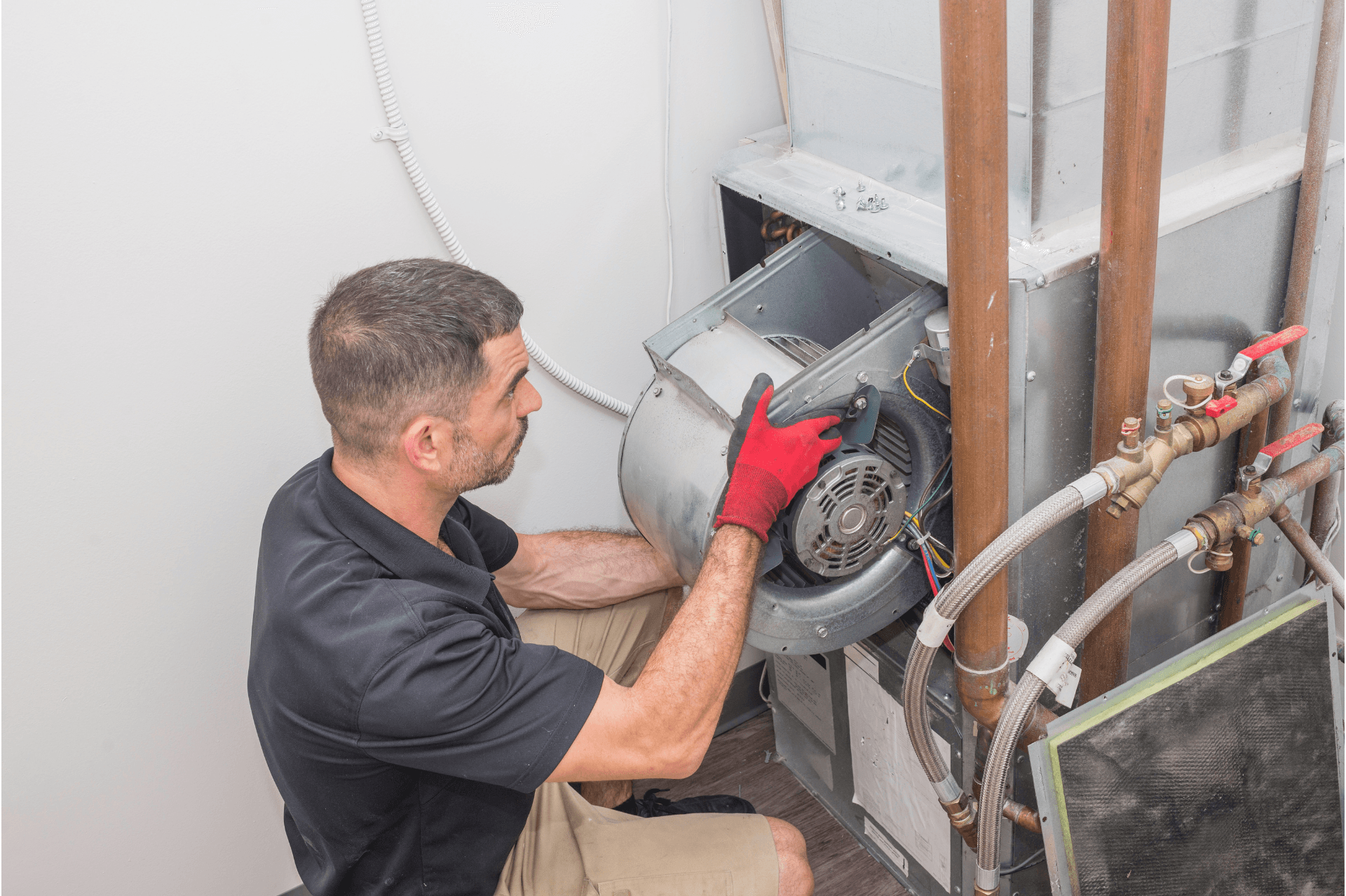 Technician wearing red gloves repairs an outdoor HVAC unit beside exposed piping.