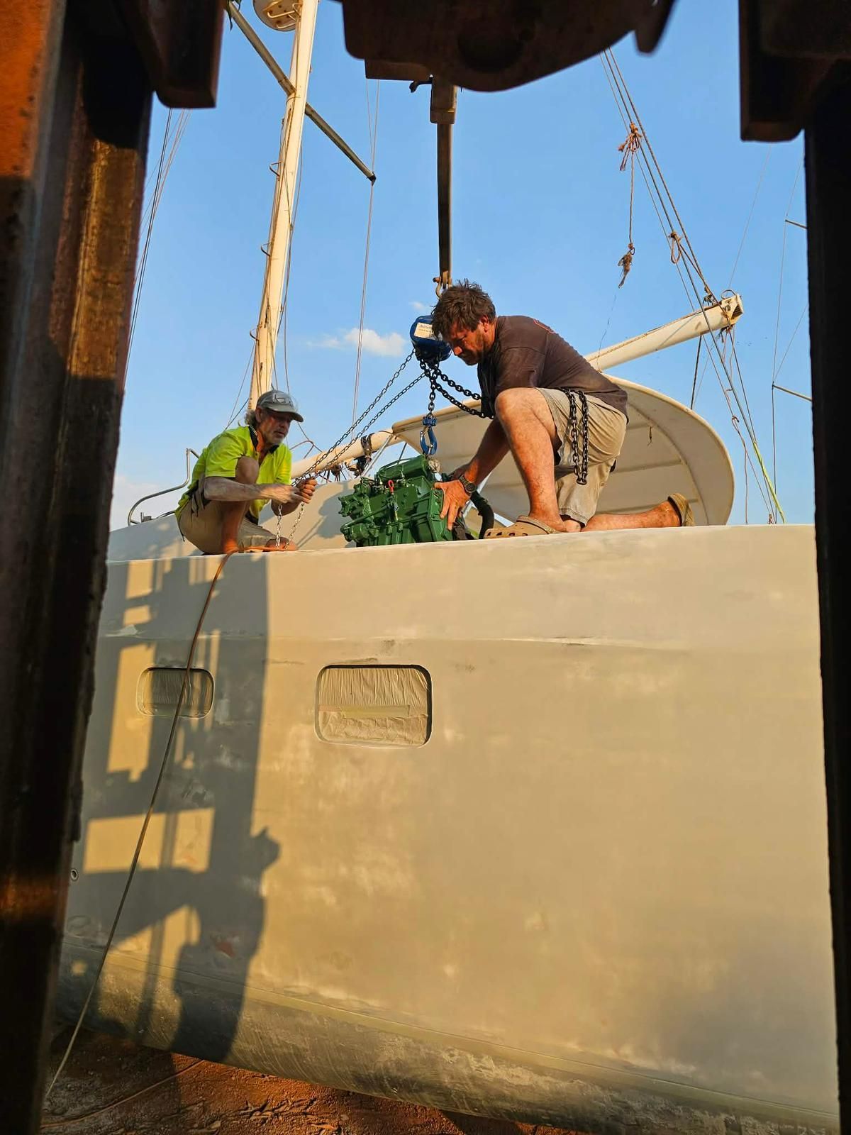 Two people work on a boat's deck, rigging a green bundle from an overhead crane. — Ocean Mate Marine Services in Coomera, QLD