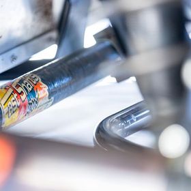Close-up of a metal bicycle frame with a colorful sticker under bright workshop lighting