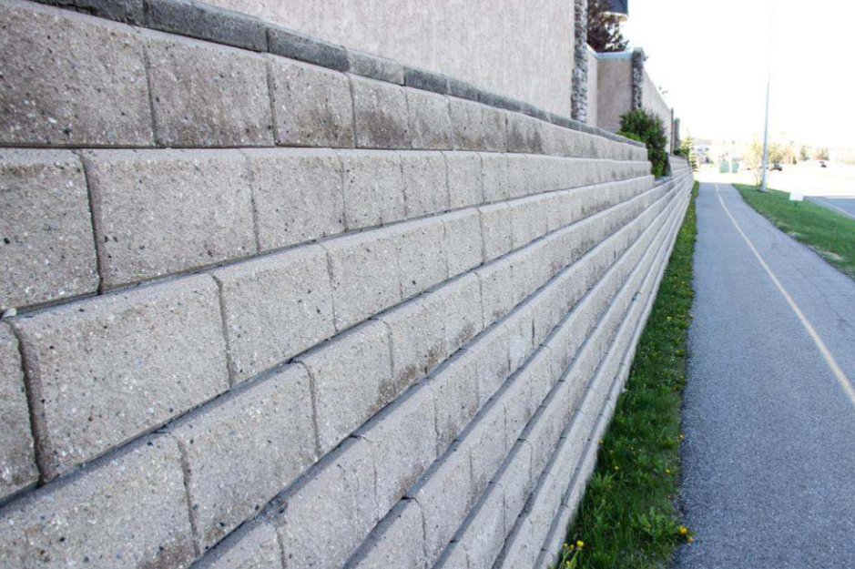 Long gray block wall beside a sidewalk and narrow grass strip on a sunny day