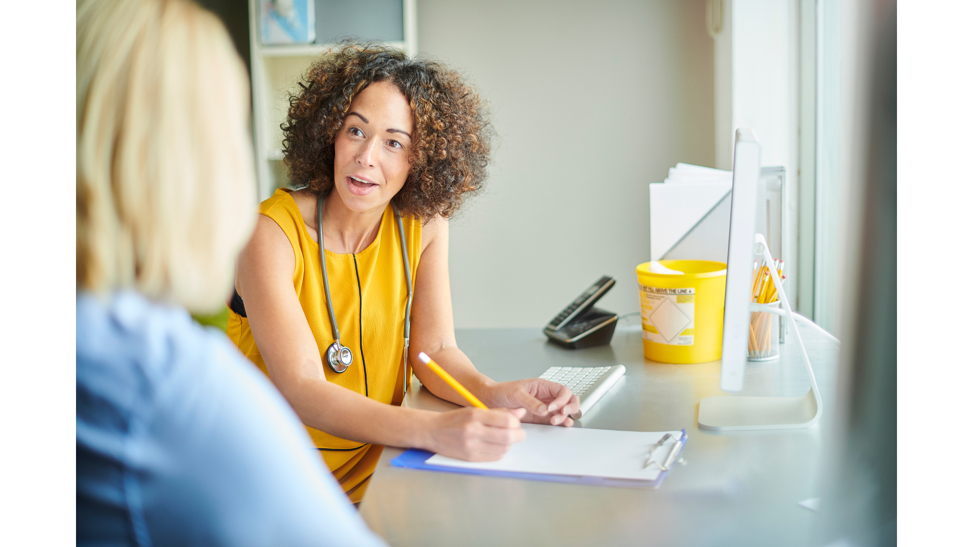 Een dokter zit aan een bureau en praat met een patiënt.