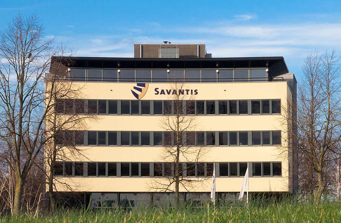 Het gele Savantis-kantoorgebouw met logo op een zonnige dag.