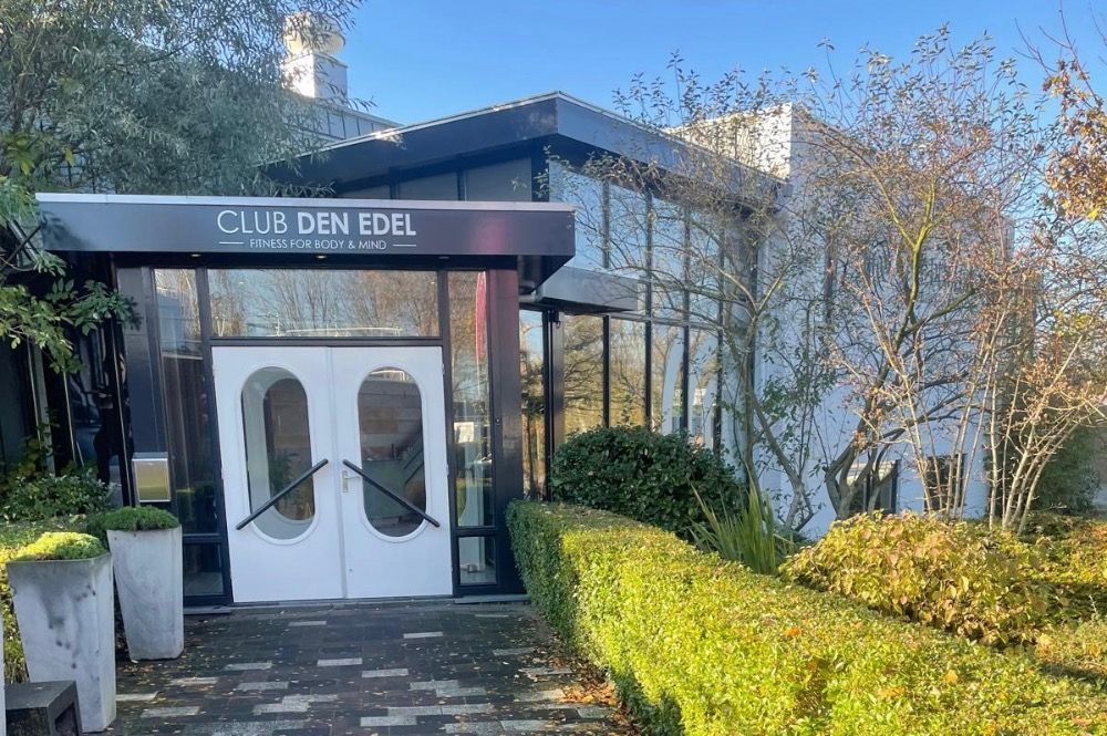 De ingang van Club Den Edel heeft glazen deuren, een zwarte luifel en groen.