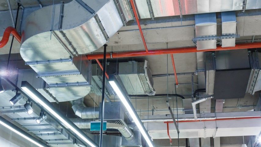 A ceiling with a lot of pipes and lights hanging from it.
