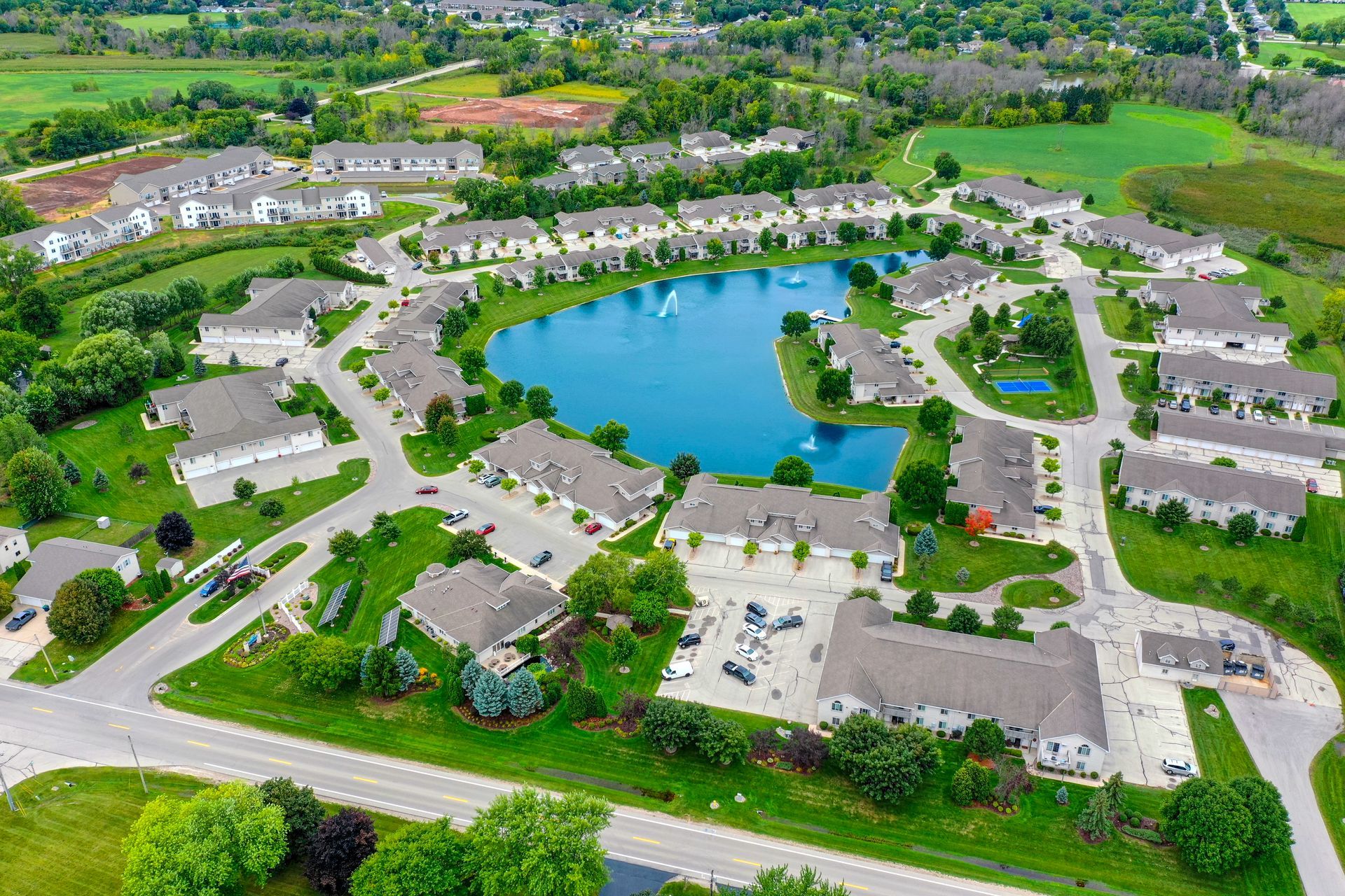 Aerial view of a suburban apartment complex surrounding a central pond with roads, lawns, and trees.