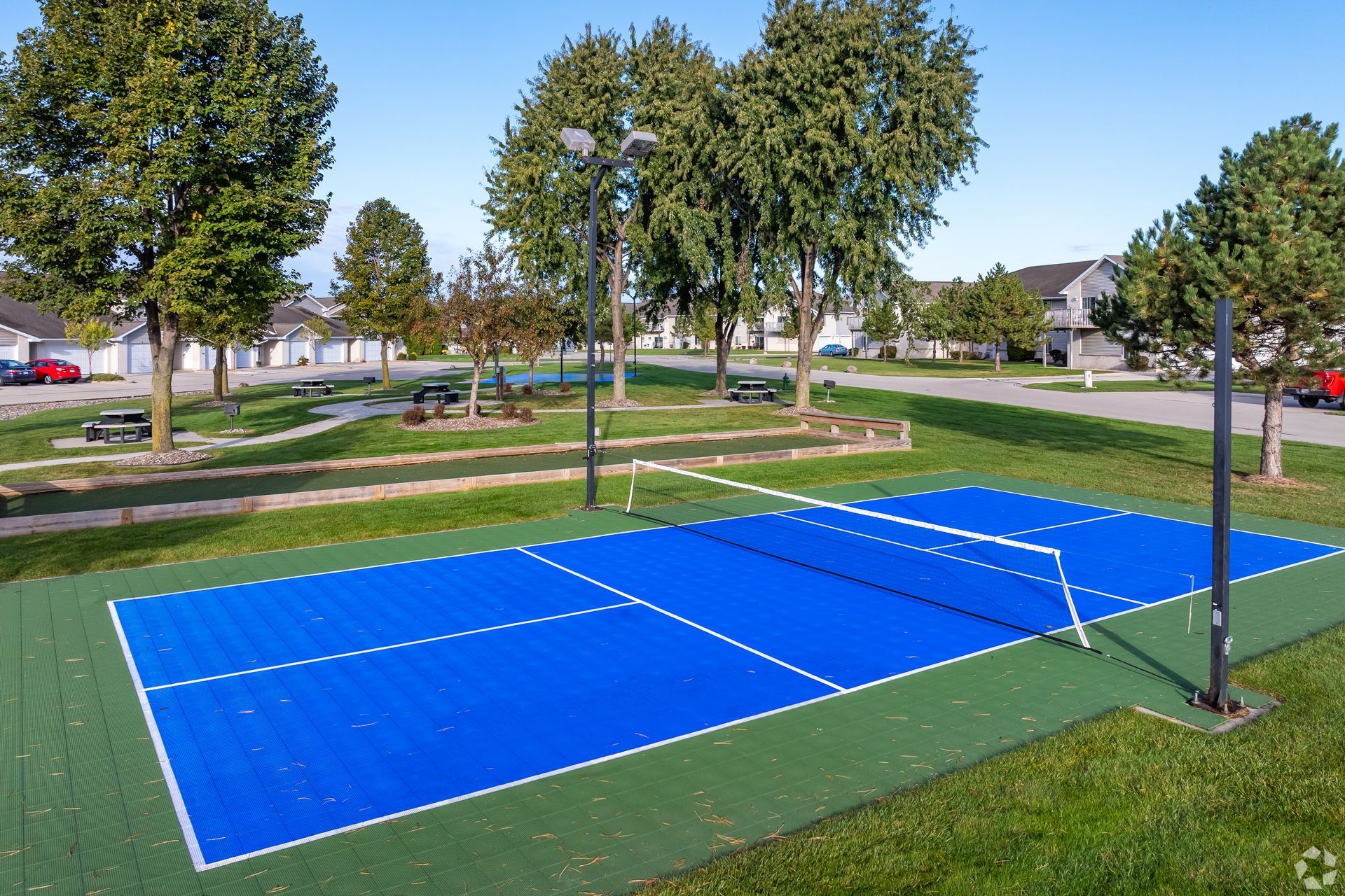 Blue outdoor sports court in a park, surrounded by grass and trees on a sunny day