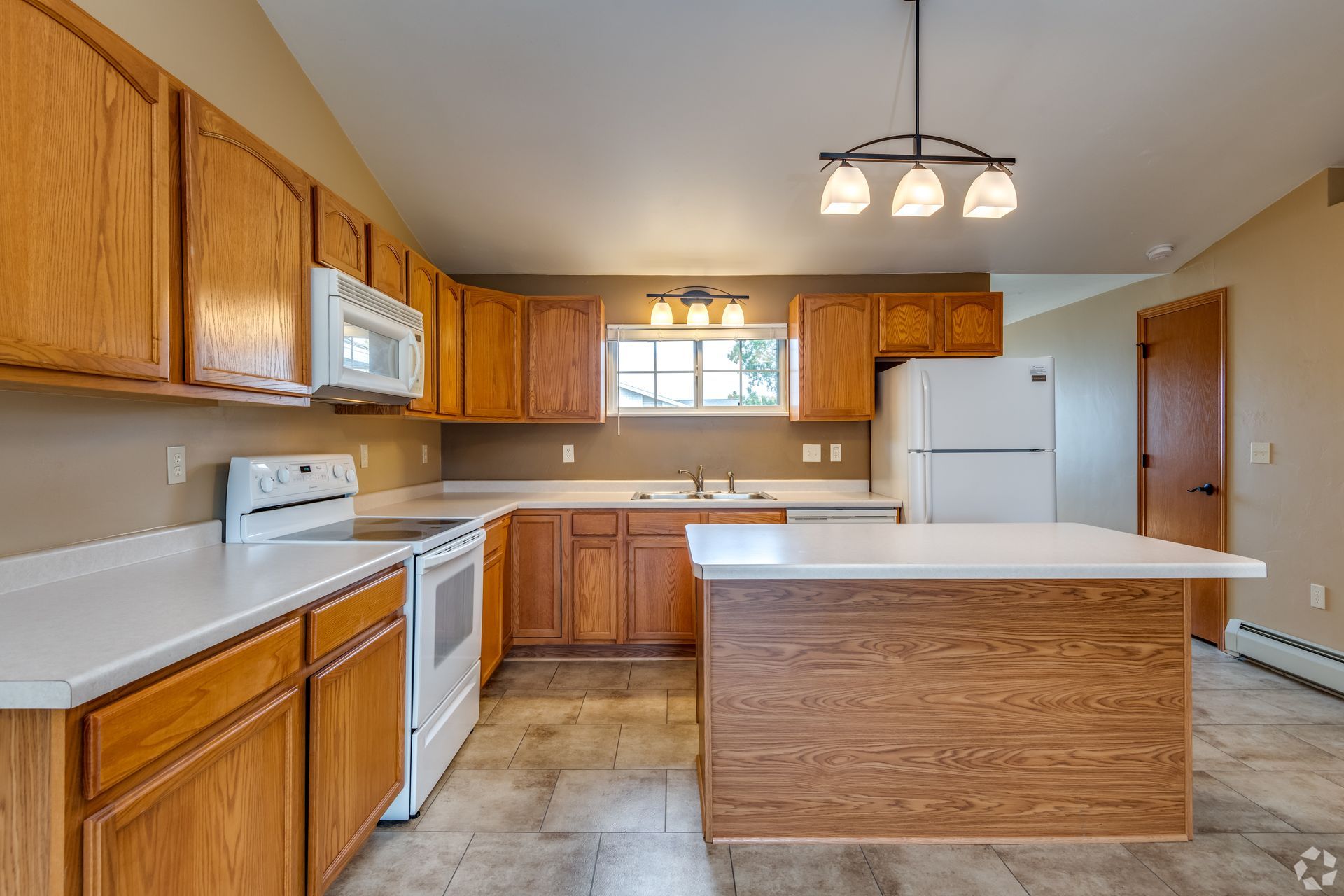 Bright kitchen with wooden cabinets, white appliances, center island, and hanging light fixture